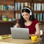 Online Education. Cheerful Korean Female Studying With Laptop And Headphones In Cafe